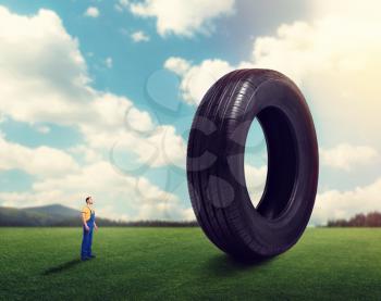 Service worker in uniform against giant tire. Repairman, wheel mounting. Tyre serviceman