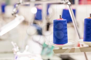 Spools of blue threads on sewing machine closeup. Cloth factory, weaving, textile production, clothing industry