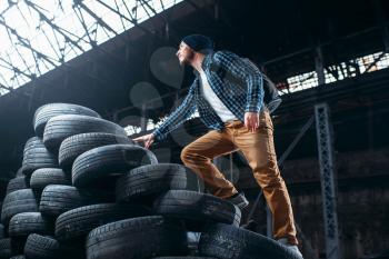 Stalker, traveler climbs a mountain of tires, abandoned factory. Danger zone, deserted place