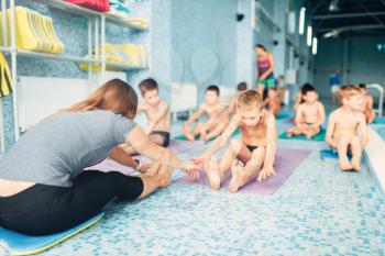 Woman instructor with children doing stretching exercises near swimming pool. Healthy and happy childhood concept. Sportive kids activity in modern sport center with pool.