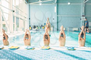 Kids doing exercise in swimming pool with hands up. Instructor shows an exercise for children. Healthy sports activity in pool. Sportive kids activity in modern sport center with pool, clean blue water.