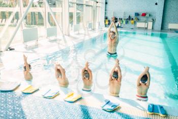 Kids doing exercise in swimming pool with hands up. Instructor shows an exercise for children. Healthy sports activity in pool. Sportive kids activity in modern sport center with pool, clean blue water.