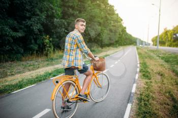 Young happy man on yellow vintage bicycle with basket, green summer park. Cycling outdoor. Male person on retro bike