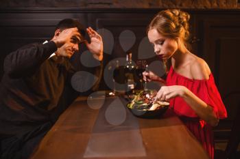 Quarrel of young couple in restaurant, bad evening. Elegant woman in red dress and her man eating in cafe