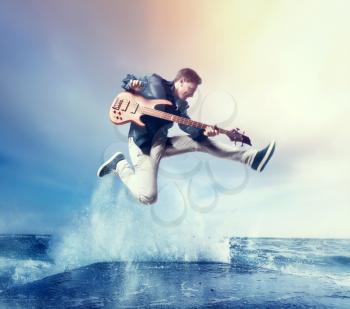 Rock guitarist with bas-guitar, snapshot in a jump, splashing water on background. Music performer