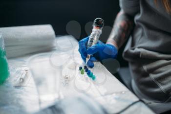 Female tattooist hands in blue sterile gloves holds tattoo machine, professional work tools on background. Tattooing in salon