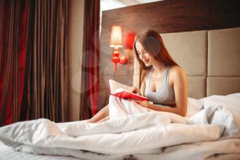 Beautiful woman in underwear reads the book in bed. Girl wake up in the morning in bedroom