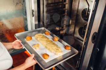 Male chef hands puts apple strudel on metal baking sheet in the oven. Sweet bakery, dessert preparation