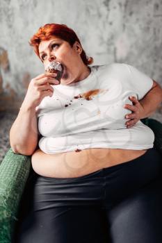 Overweight woman sits in a chair and eats sweet cake, laziness and obesity, bulimic. Unhealthy food eating, fatty female