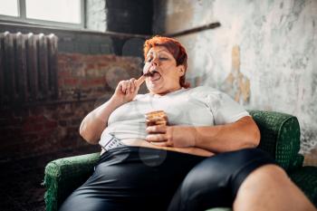 Overweight woman sits in a chair and eats sweets. Unhealthy lifestyle, obesity