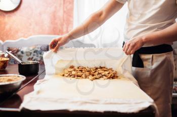 Male chef wraps the filling into dough, apple strudel preparation process. Homemade sweet dessert