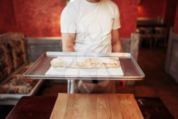 Male chef holds metal baking sheet with classical apple strudel, bakery cooking. Homemade sweet dessert, preparation process