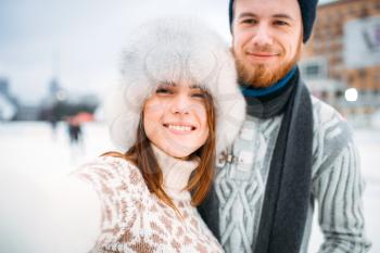 Young love couple, selfie on skating rink. Winter ice-skating on open air, active leisure, man and woman skates together