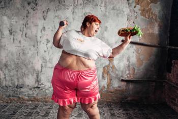 Overweight woman with dumbbell and sandwich in hands, fight against obesity concept, overweight problem. Junk food eating