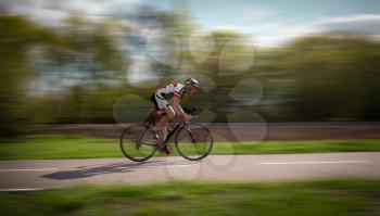 Cyclist in helmet and sportswear rides on bicycle, speed effect, side view. Workout on bike path, cycling training on asphalt road