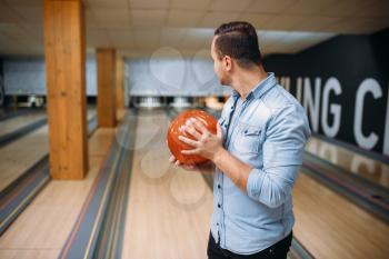 Male bowler standing on lane and poses with ball in hands, back view. Bowling alley player prepares to throw strike shot in club, active leisure