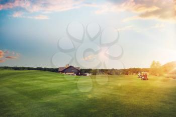 Golf cars on trimmed lawn, game course at sunset. Golfers on green meadow in sport club, golging playground