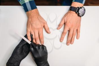 Female master in black gloves polishing nails to male client, top view, men manicure in salon. Manicurist doing hands care procedure