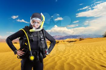 Diver in wetsuit and diving gear standing in desert. Frogman in mask and scuba swims in the ocean