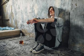 Junkie with syringe in hand sitting on the floor after dose, bottle of alcohol is near. Drug addiction concept, narcotic addicted people