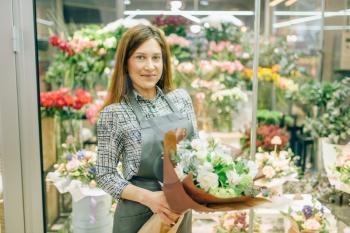 Female florist in apron with fresh bouquet in flower shop, floral business concept