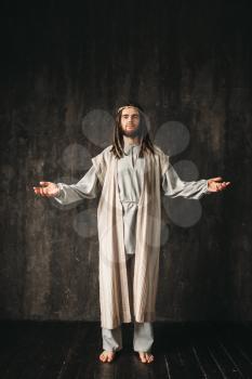 Jesus Christ in white robe praying with open arms, dark background. Son of God, christian faith