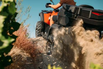 Atv rider climbing the sand mountain in quarry, back view, dust clouds. Male driver in helmet on quad bike, offroad in sandpit
