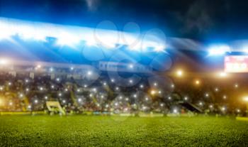 Football stadium, tribunes with fans, shiny lights, view from field. Green grass turf on playground