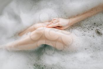 Nude legs of female person lying in bath with foam, top view. Relaxation, health and skin care in bathroom, spa
