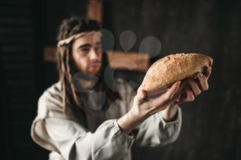 Jesus Christ with bread in hands, sacred food, crucifixion cross on background. Son of God, christian faith symbol