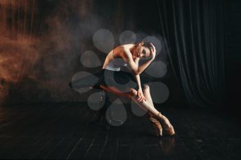 Ballerina sitting on black banquette on the stage in theatre. Elegance ballet dancer poses in class