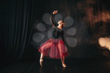 Ballet dancer in red dress dancing on the stage in theatre. Graceful ballerina training in class
