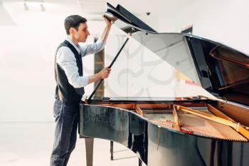 Male pianist opens the lid of the black grand piano. Musician adjusts royale, classical musical instrument tuning
