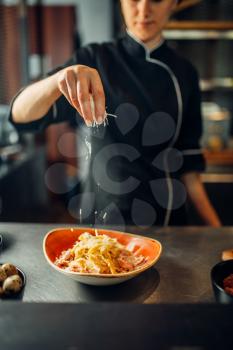 Female chef cooking pasta with cheese in a bowl on wooden table. Garnish for stek, food preparation on kitchen