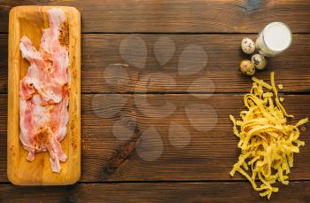Piece of raw meat in seasoning, pasta and eggs on wooden table, top view, nobody. Uncooked fresh stek, food preparation, cooking