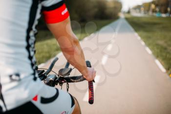 Cyclist in helmet and sportswear rides on bicycle, back view. Workout on bike path, cycling