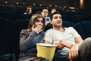 Couple with popcorn fascinated watching the film in cinema. Showtime, entertainment industry
