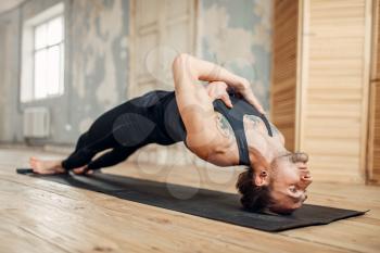 Male yoga standing on hands, balance and press training. Fitness exercise in gym with grunge interior. Fit workout indoors