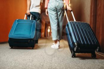 Couple with suitcase walking by the hotel corridor. Travelling or tourism concept. Tourists with bags in hallway