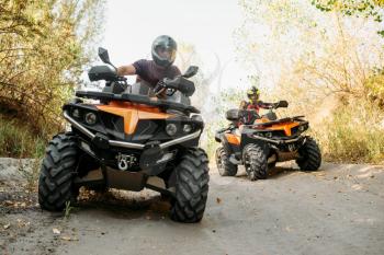 Two quad bike riders in helmets travels in forest, front view. Riding on atv, extreme sport and travelling, quadbike adventure