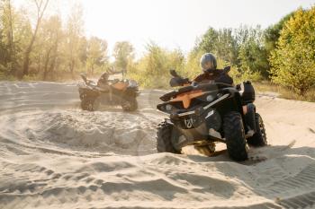 Two atv riders in helmets ride in a circle on sand, offroad in forest. Riding on quad bike, extreme sport and travelling, quadbike summer adventure