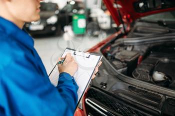 Technician with notebook fills the check list, car with opened hood, fixing the problems. Automobile service, vehicle maintenance