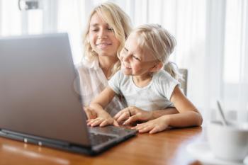 Smiling mother and child uses laptop at home. Parent feeling, togetherness, happy family