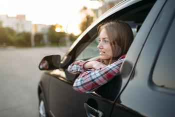 Smiling female driver beginner looks out of the car window. Woman in vehicle, driving automobile concept