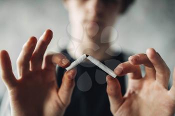 Addicted male person breaks a cigarette, blur background. Smoking addiction concept