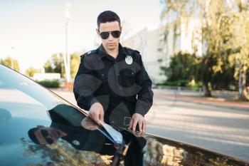 Male policeman in uniform writes a fine on the road. Law protection, car traffic inspector, safety control job