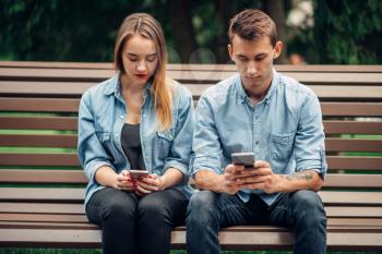 Phone addiction, addict couple using smartphones on the bench in park, social addicted people