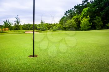 Final hole with flag on golf course with green trimmed grass, nobody. Meadow in sport club, lawn for game, empty playground