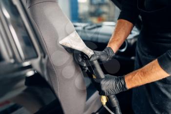 Professional dry cleaning of car seats with vacuum cleaner. Carwash service, male worker in gloves removes dust