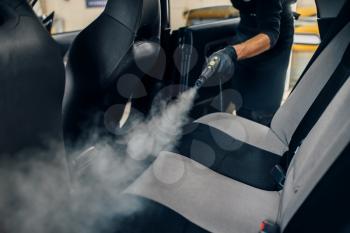 Carwash service, male worker in gloves cleans seats with steam cleaner. Professional dry cleaning of car interior
